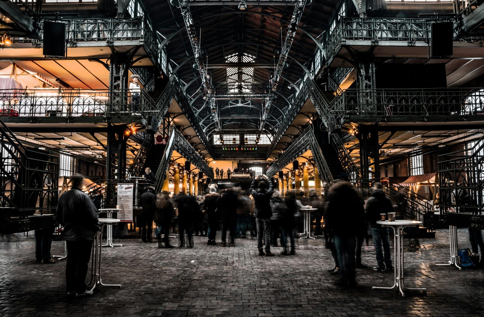 Busy indoor market with vintage iron architecture and bustling crowd, capturing urban commerce.